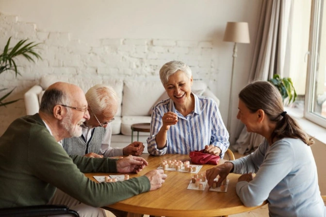 Group of seniors laughing and playing a game together at a wooden table