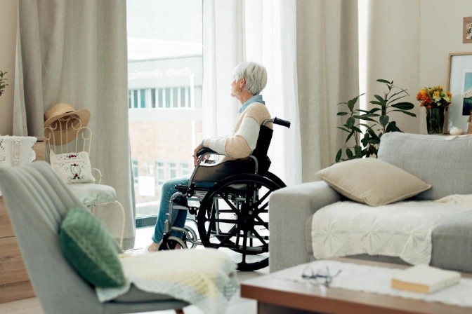 Senior woman in a wheelchair gazing out the window inside a cozy apartment